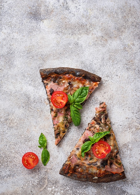 Pedaços de pizza preta com tomate e manjericão