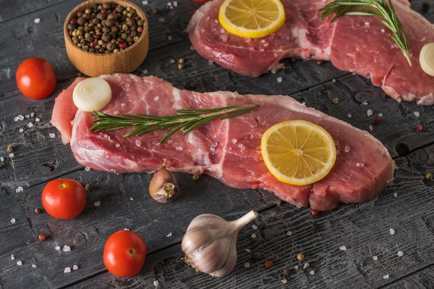 Pedaços de porco com limão, pimenta e ervas em uma mesa de madeira. Ingredientes para cozinhar pratos de carne.