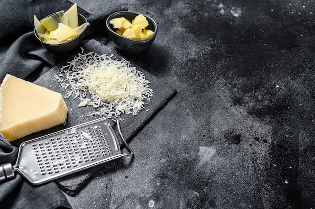 Pedaços de queijo duro parmigiano reggiano. Fatia, corte, ralado. Fundo preto. Vista do topo. Copie o espaço