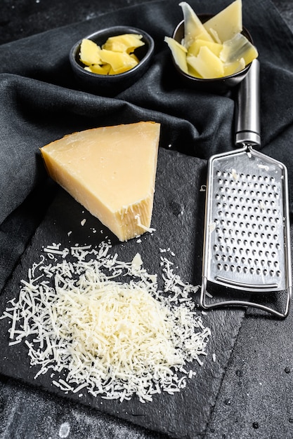 Pedaços de queijo duro parmigiano reggiano. fatiar, cortar, ralado. fundo preto. vista do topo.