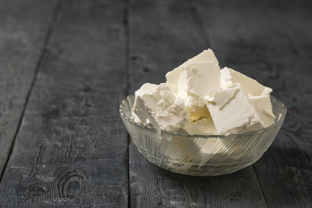 Pedaços de queijo feta em uma tigela de vidro sobre uma mesa preta rústica. Queijo natural de leite de ovelha.