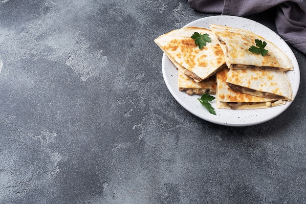 Pedaços de quesadilla com creme de leite cogumelos e queijo em um prato com folhas de salsa.