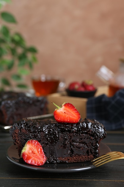 Pedazo de bizcocho de chocolate sabroso con fresas en primer plano de la mesa de madera negra