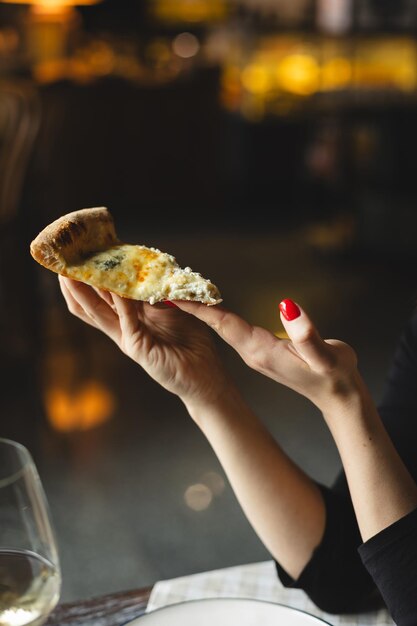 Foto un pedazo de deliciosa pizza en las manos sobre un fondo oscuro