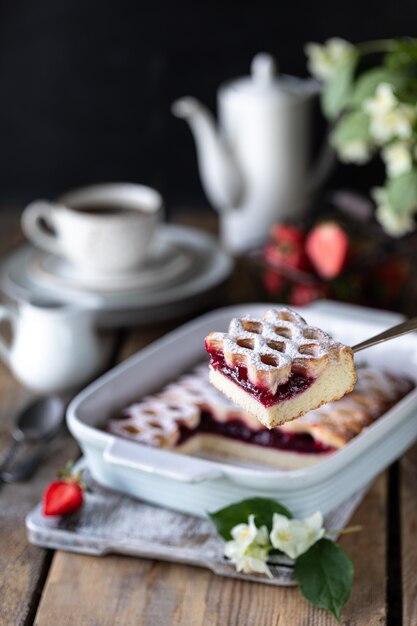 Pedazo de delicioso pastel de bayas con fresas con una taza de café para el desayuno.