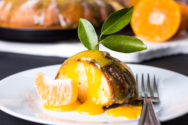 Pedazo de delicioso pastel de mandarina con almíbar cremoso en la placa blanca sobre la mesa de madera de carbón