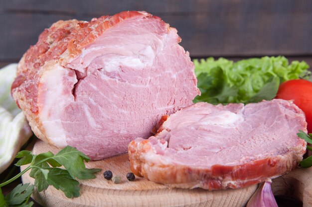 Un pedazo de jamón y de verduras en un fondo de madera. Producto de la carne