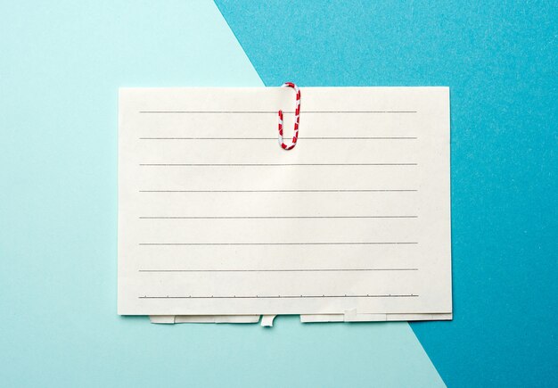 Pedazo de papel blanco en una línea y un clip rojo sobre un fondo azul.