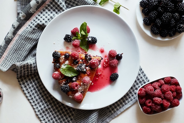 Pedazo de pastel con arándanos, frambuesa y menta de postre en una placa blanca, servilleta