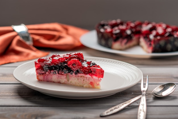 Pedazo de pastel con bayas frambuesa grosella fresa sobre una placa blanca junto a la cuchara de postre y