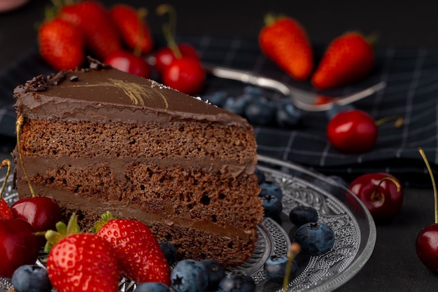 Pedazo de pastel de chocolate con bayas en placa de vidrio sobre mesa oscura