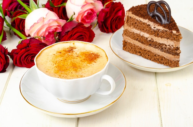 Pedazo de pastel de chocolate, capuchino, flores en la mesa.