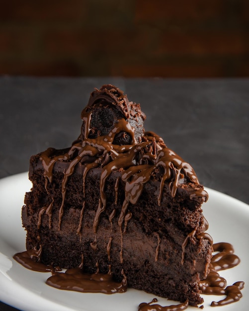 Pedazo de pastel de chocolate con jarabe de chocolate, fondo negro, pared de ladrillo