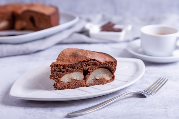 Pedazo de pastel de chocolate con pera En el fondo hay un pastel una taza de café y trozos de chocolate Primer plano