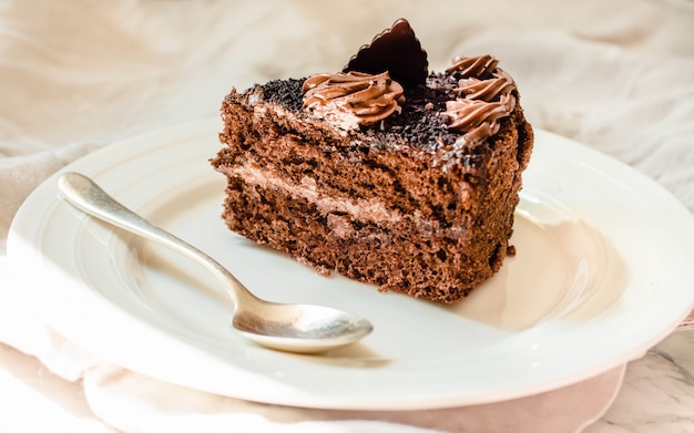 Pedazo de pastel de chocolate en un plato blanco y una taza de café de oro, primer plano. Enfoque selectivo Concepto de ambiente de comida dulce y parientes