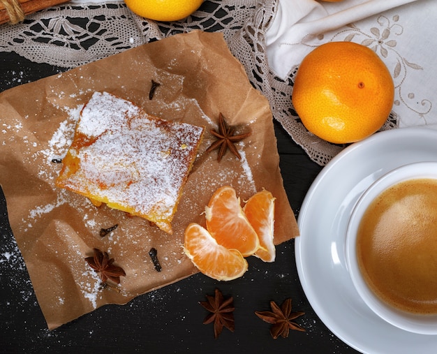 Pedazo de pastel de mandarina con azúcar en polvo y una taza de café blanca