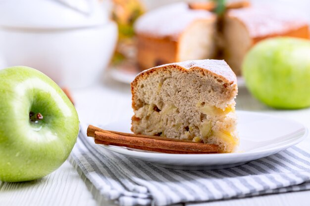 Un pedazo de pastel de manzana casero charlotte en un plato servido con palitos de canela y una ramita de menta