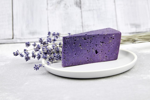 Pedazo de queso de lavanda con albahaca seca y flores de lavanda en placa sobre mesa de hormigón