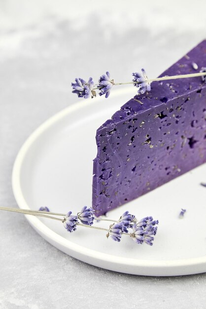 Un pedazo de queso de lavanda con albahaca seca y flores de lavanda en un plato en una mesa de hormigón gris