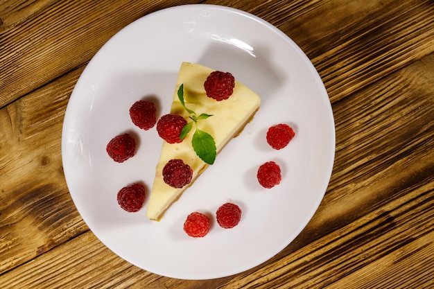 Pedazo de sabroso pastel de queso de Nueva York con frambuesas en un plato blanco sobre la mesa de madera. Vista superior