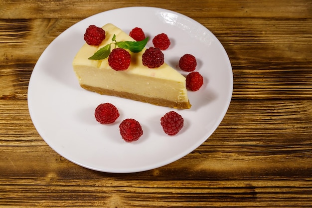 Pedazo de sabroso pastel de queso de Nueva York con frambuesas en un plato blanco sobre una mesa de madera