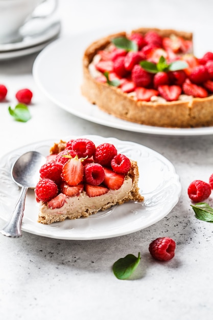 Pedazo de tarta de bayas con frambuesas, fresas y crema en un plato blanco