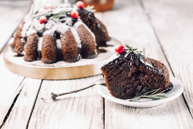 Pedazo de tarta de chocolate navideña adornado con bayas y romero en una placa