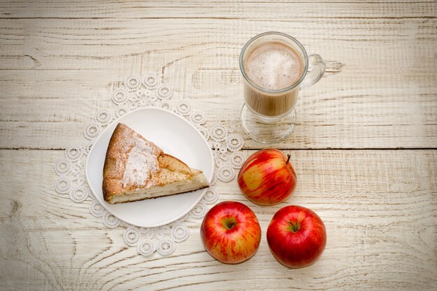 Pedazo de tarta de manzana, capuchino y manzanas maduras en una mesa de madera clara, vista superior