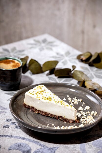 Pedazo de tarta de queso vegana cruda, sin hornear sin gluten, decorada con ralladura de limón y anacardos en la placa