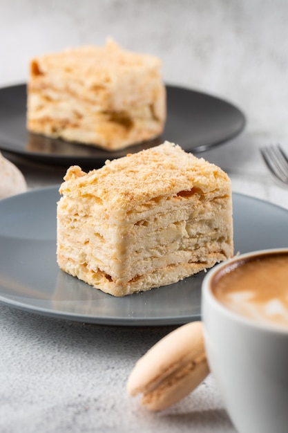 Pedazo de torta Napoleón en la placa azul en el fondo de mármol, visión ascendente cercana. Postre tradicional de milhojas con hojaldre y crema pastelera, copie el espacio. Foto vertical. Foto del menú de panadería.