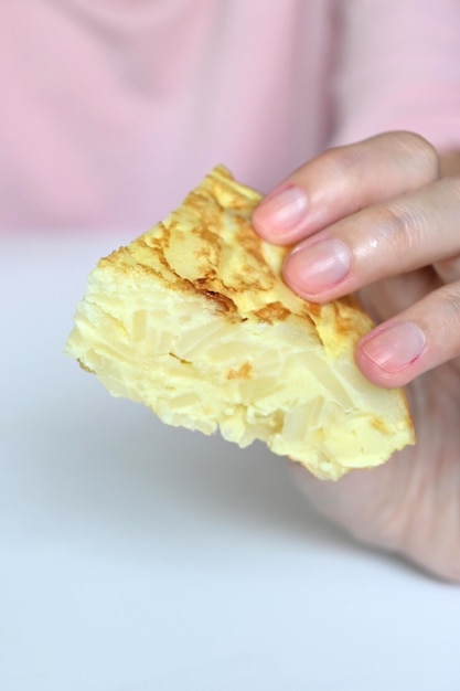 Pedazo de tortilla española sosteniendo por mano de mujer, espacio de copia y enfoque selectivo