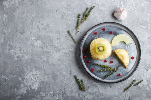 Pedazos de cerdo cocido con la piña, el queso y el kiwi en la placa gris.