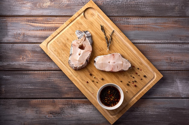 Pedazos de pimiento romero adobo de pescado crudo blanco en rodajas sobre tabla de cortar de madera rústica