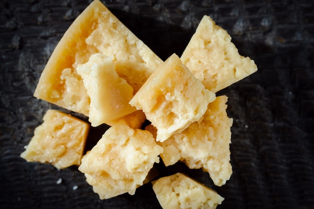 Pedazos de queso parmesano en un fondo de madera oscuro.