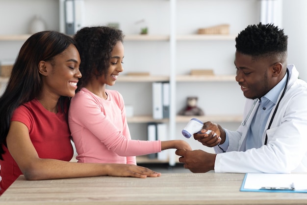 Pediatra afro-americano verificando a temperatura corporal da menina