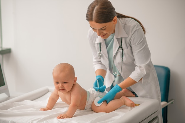 Pediatra com luvas descartáveis de nitrila administrando uma injeção intramuscular na parte externa da coxa de um recém-nascido