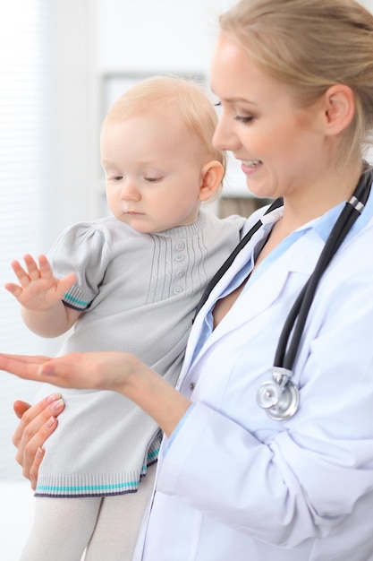 El pediatra está cuidando al paciente en el hospital. La doctora sostiene a una niña pequeña en las manos. Concepto de atención médica, seguro y ayuda.