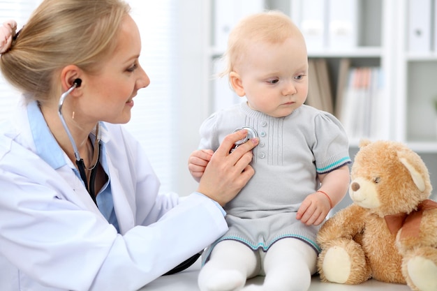 Pediatra está cuidando do bebê no hospital. A menina está sendo examinada pelo doutor com estetoscópio. Cuidados de saúde, seguro e conceito de ajuda.