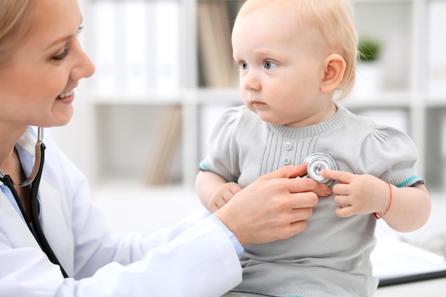 Pediatra está cuidando do bebê no hospital. A menina está sendo examinada pelo doutor com estetoscópio. Cuidados de saúde, seguro e conceito de ajuda.