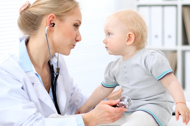 Pediatra está cuidando do bebê no hospital. A menina está sendo examinada pelo doutor com estetoscópio. Cuidados de saúde, seguro e conceito de ajuda.