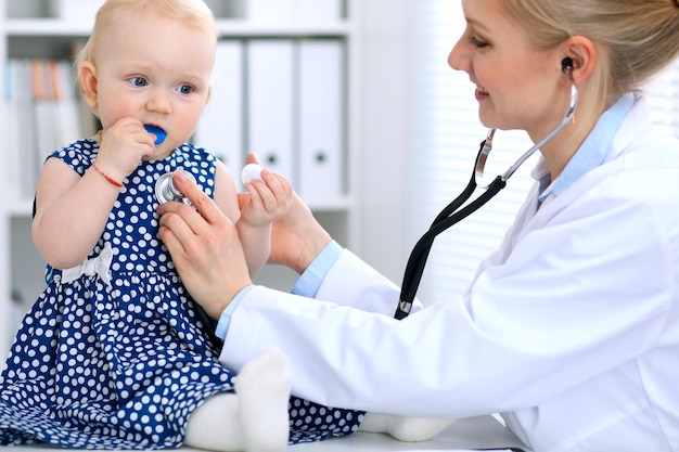 Pediatra está cuidando do bebê no hospital. A menina está sendo examinada pelo doutor com estetoscópio. Cuidados de saúde, seguro e conceito de ajuda.