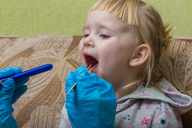 El pediatra examina la garganta de una niña enferma Visita domiciliaria