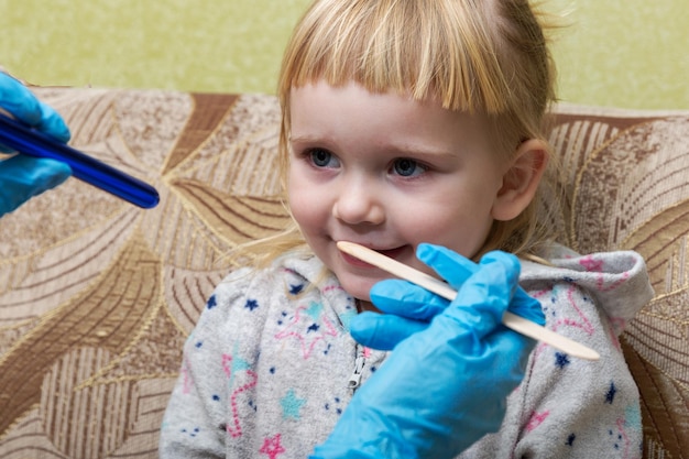 El pediatra examina la garganta de una niña enferma Visita domiciliaria