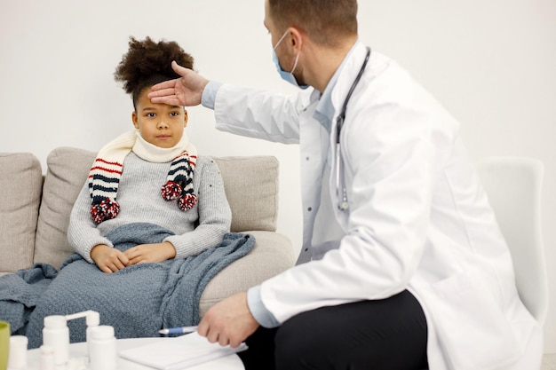 Pediatra masculino sosteniendo la mano en la frente de una niña negra enferma