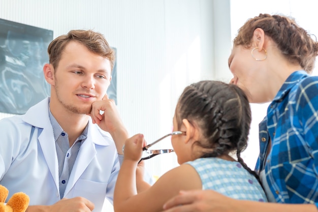 Pediatra (médico) homem examinar paciente menina usando um estetoscópio no hospital.