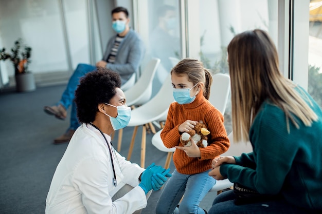 Pediatra negra hablando con madre e hija en una sala de espera durante la pandemia del coronavirus