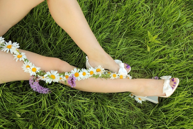 Pedicura con una capa lila mate en una niña sentada sobre la hierba verde con un arreglo floral de margaritas en los pies.