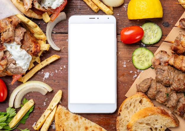 Pedido en línea de Gyro pita shawarma Dos envolturas con carne y teléfono móvil con pantalla en blanco en una mesa de madera