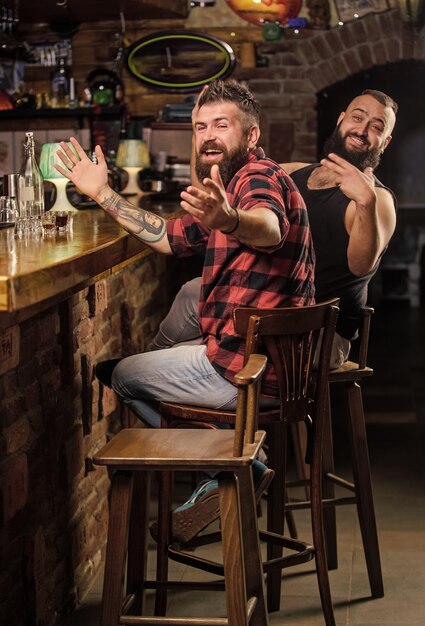 Pedir bebidas no balcão do bar Homem barbudo brutal hipster passa lazer com amigo no balcão do bar Homens relaxando no bar Sexta-feira relaxamento no bar Amizade e lazer Amigos relaxando no pub