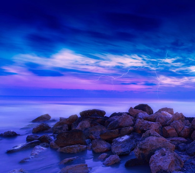 Pedras ao lado do mar contra o céu azul durante o pôr-do-sol